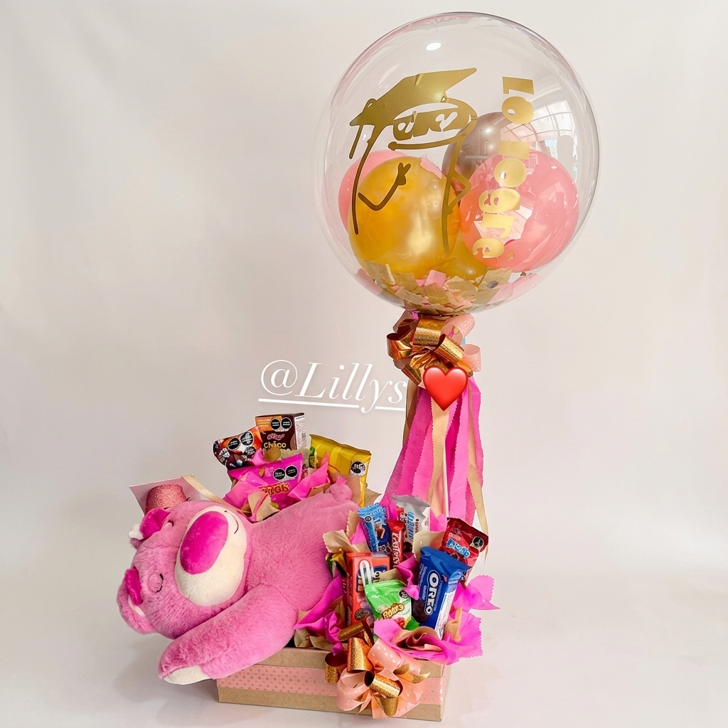 Caja repleta de golosinas con peluche rosa y globo.